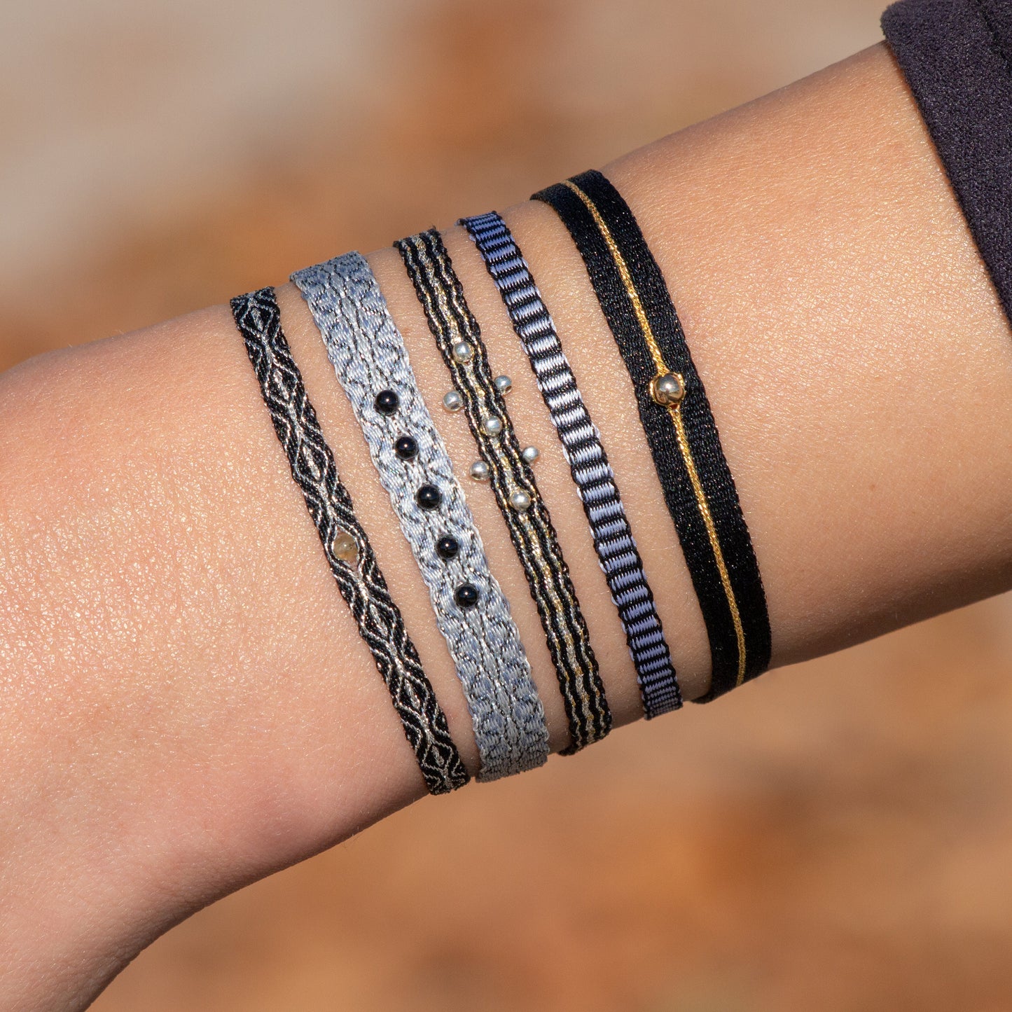 Bracelets bohème-chic tissés main en tons noir, gris et doré, avec petites perles argentées et dorées, portés au poignet, création artisanale Ethchic.