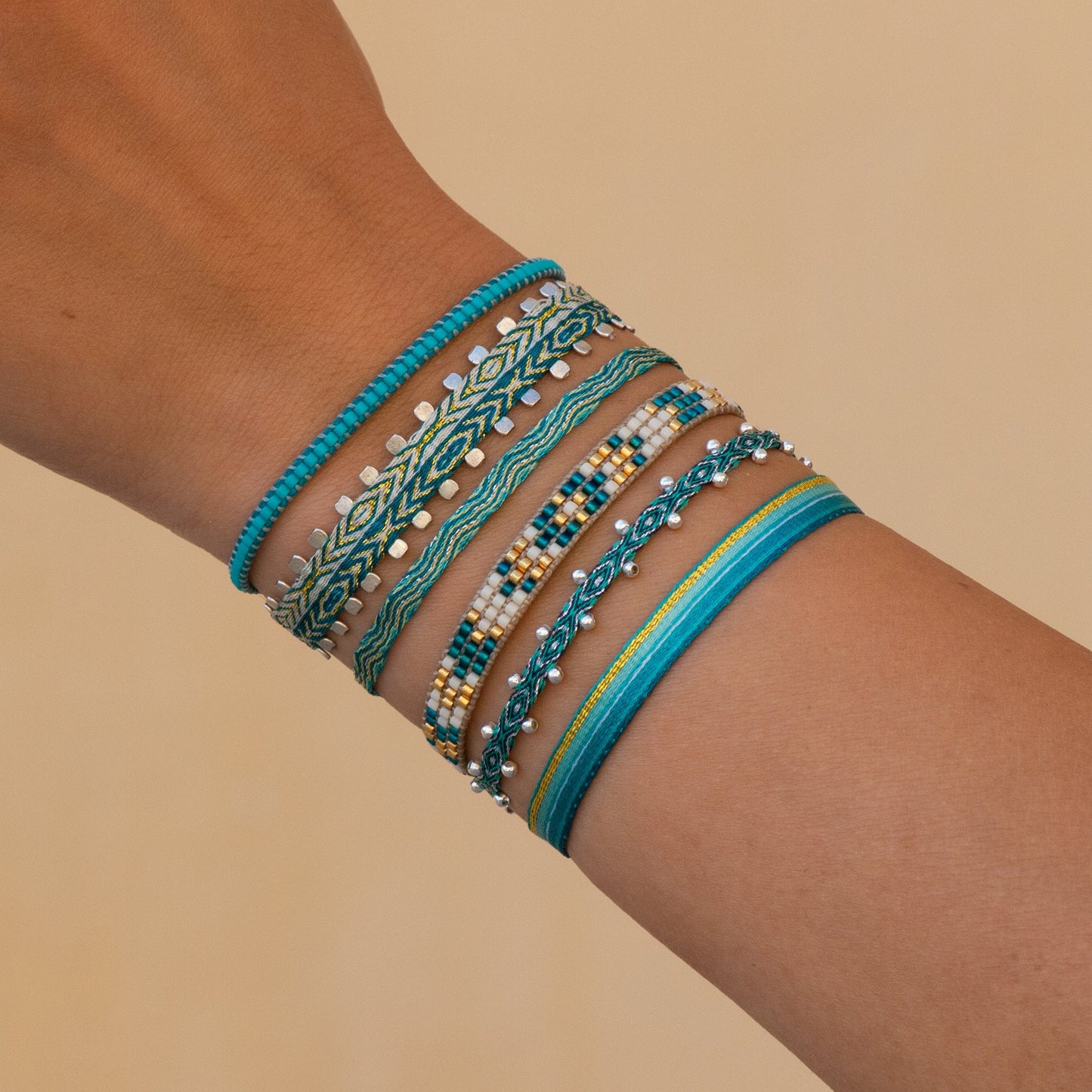 Ensemble de bracelets bohème-chic tissés main en tons turquoise, doré et vert, portés au poignet, création Ethchic. Perles en argent. Waterproof.