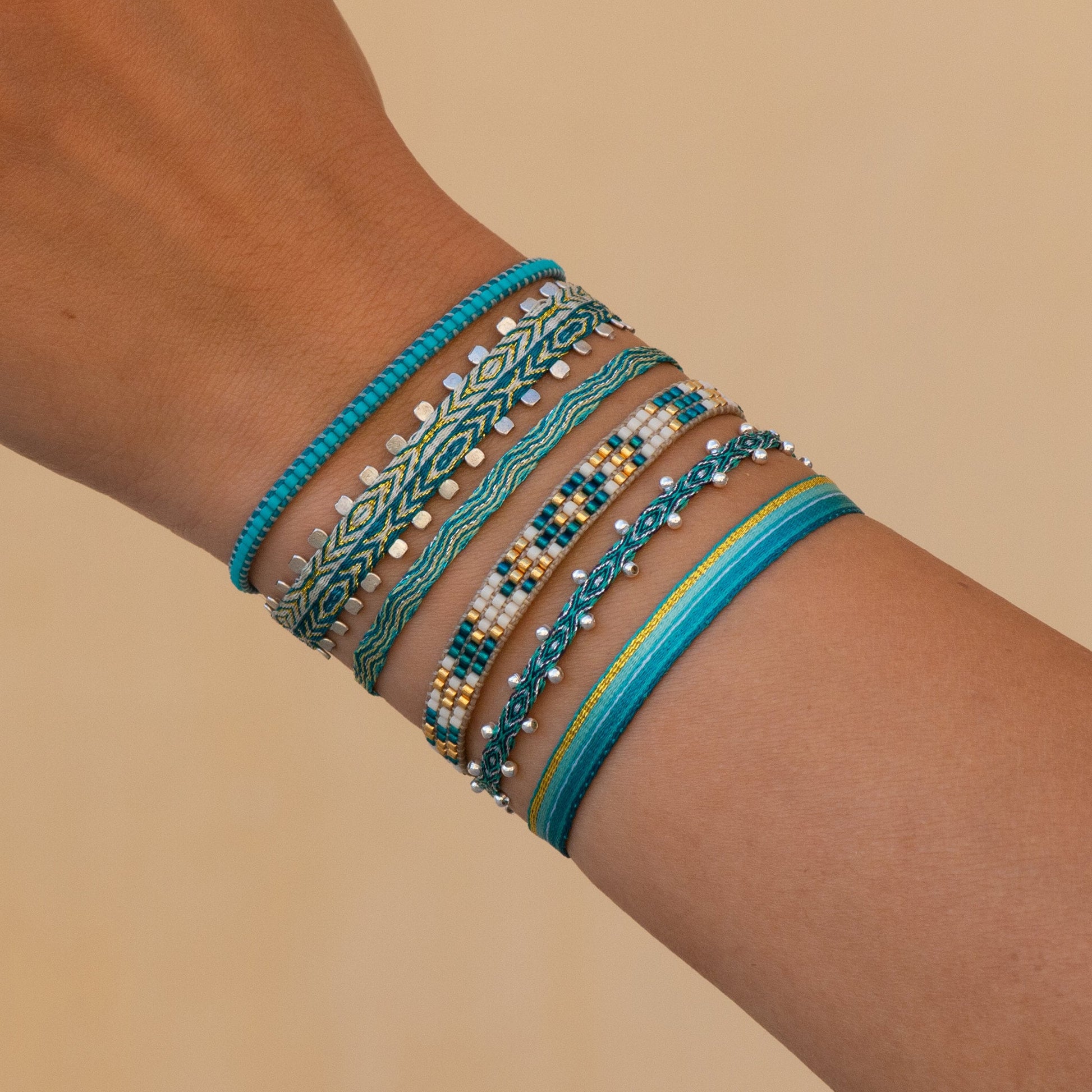 Ensemble de bracelets bohème-chic tissés main en tons turquoise, doré et vert, portés au poignet, création Ethchic. Perles en argent. Waterproof.